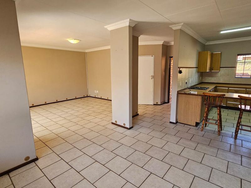 Spacious open-plan living and kitchen area featuring ceramic tile flooring, built-in cabinetry, and a central structural pillar, offering a versatile layout for modern living.