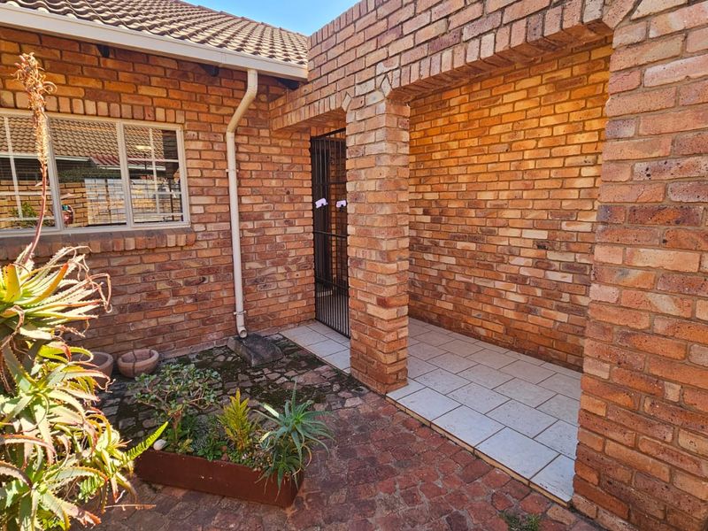 A private rear courtyard featuring face brick walls, a covered tiled patio area, and a secure entrance gate.
