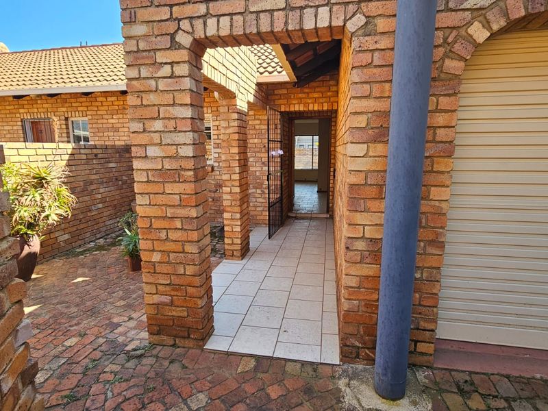 A front entrance area featuring a face brick facade, tiled walkway, and a secure roller garage door leading into the property.