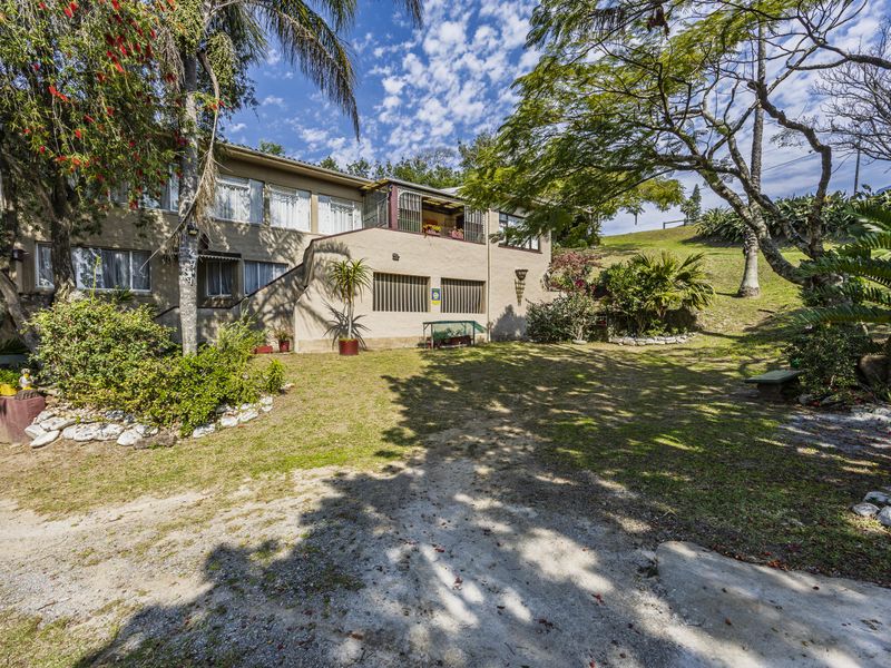 Rear view of the house featuring a balcony, security bars on lower windows, and a spacious established garden with mature trees.