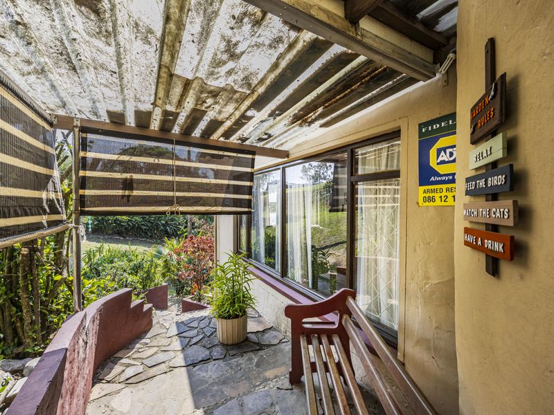 A covered outdoor patio area featuring stone paving and a corrugated roof, providing direct access to the garden through sliding glass doors.