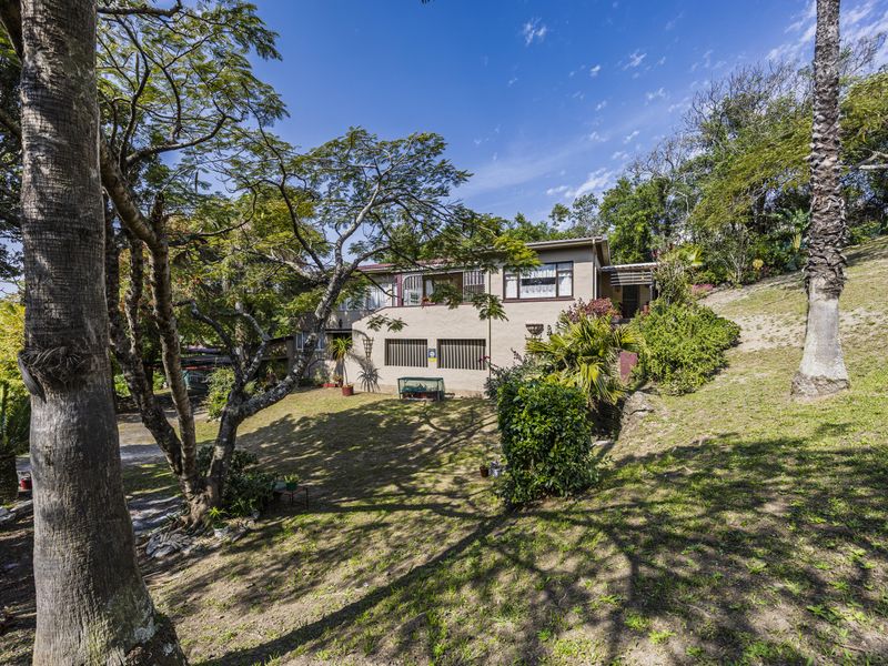 Rear view of the house featuring a spacious garden, mature trees, and a multi-level exterior facade with security bars on windows.