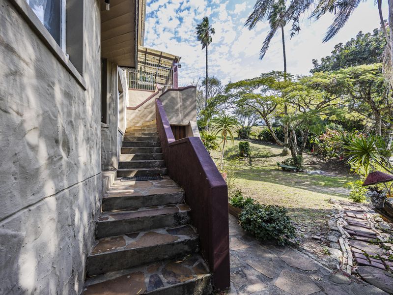 Exterior rear view featuring a stone-clad staircase leading to an elevated area, adjacent to a landscaped garden and paved pathway.
