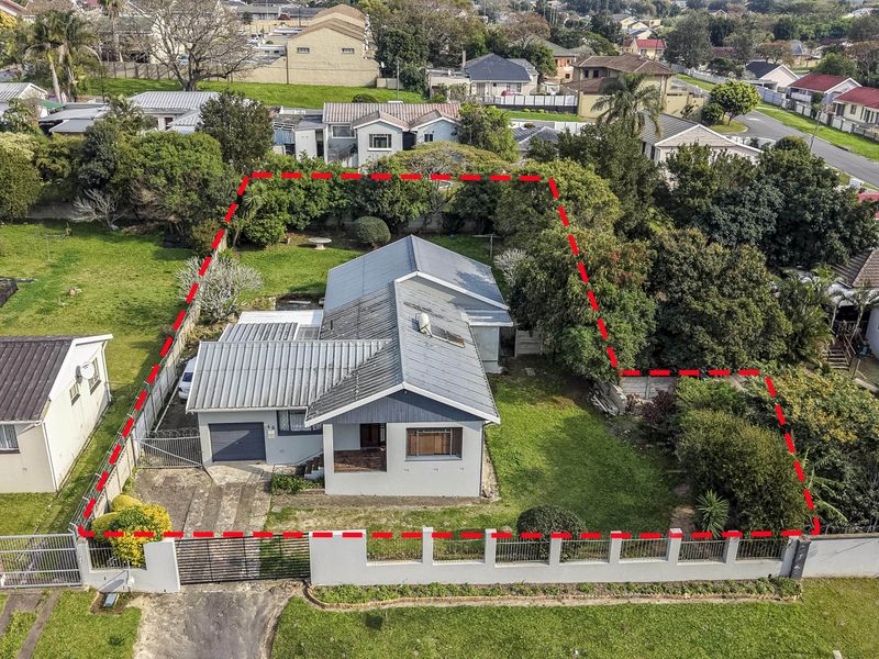 Aerial view of a residential property featuring a metal roof, concrete driveway, and a large garden area enclosed by a perimeter wall.