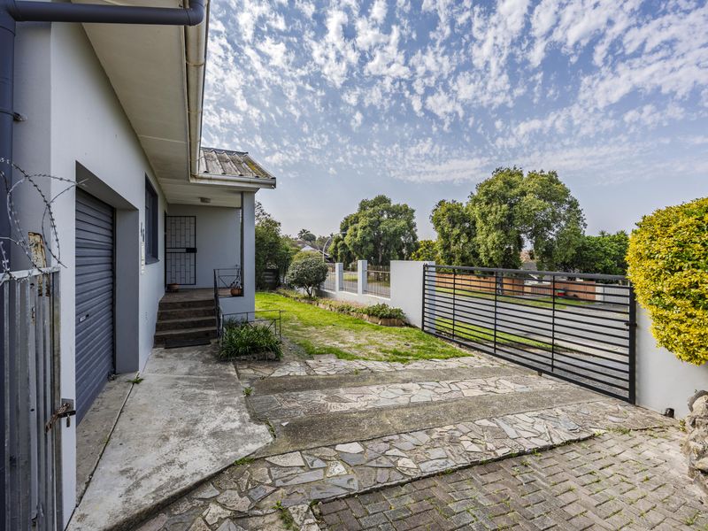 Front exterior view featuring a paved driveway, garage access, and secure boundary wall with gate.