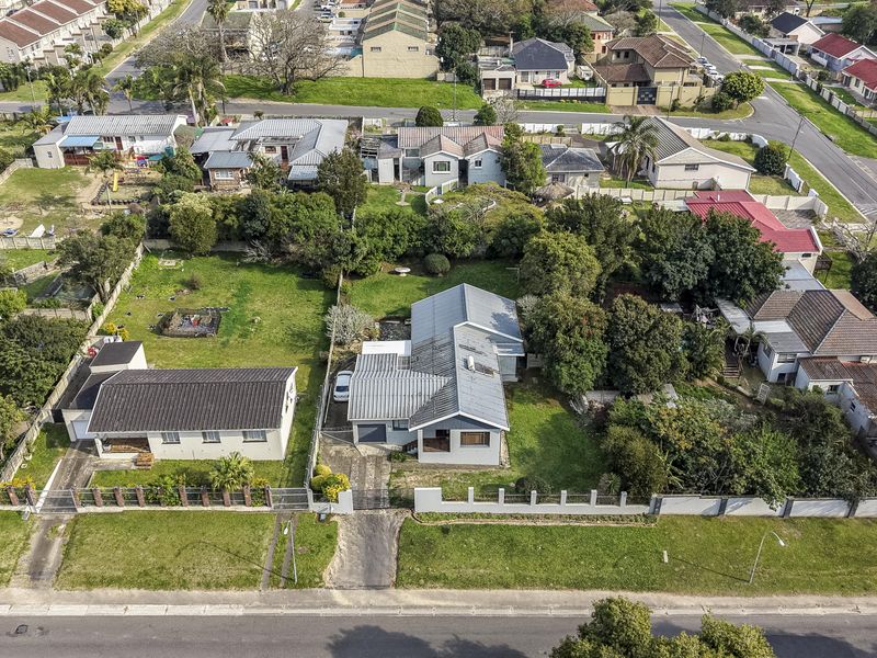 Aerial view of a residential property featuring a metal roof, paved driveway, and established garden within a suburban neighborhood setting.