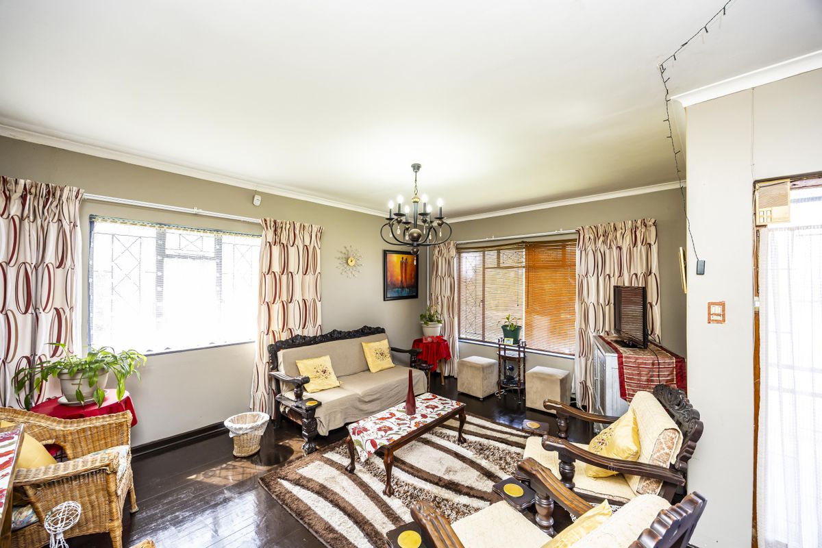A spacious living room featuring dark timber flooring, decorative cove cornicing, and large windows fitted with security burglar bars.