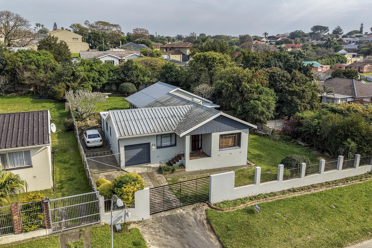 Aerial view of a residential property featuring a metal roof, gated driveway, and established garden in a suburban neighborhood.