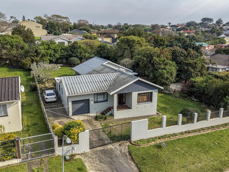 Aerial view of a residential property featuring a metal roof, gated driveway, and established garden in a suburban neighborhood.