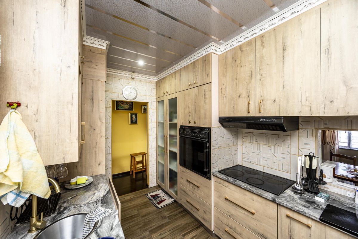 A functional kitchen featuring light wood-tone cabinetry, stone countertops, integrated oven, electric cooktop, and decorative ceiling finishes.