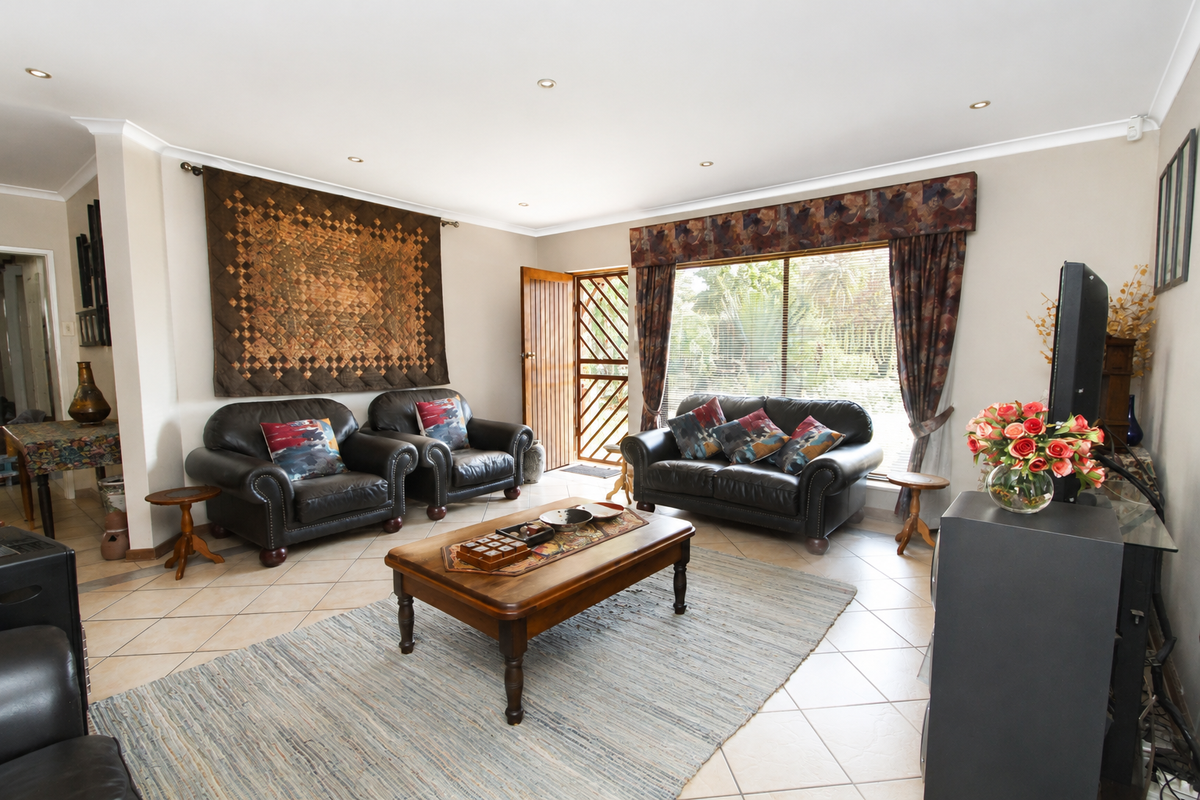 A spacious living room featuring tiled flooring, recessed downlighting, and a large window with a security gate leading to the exterior.