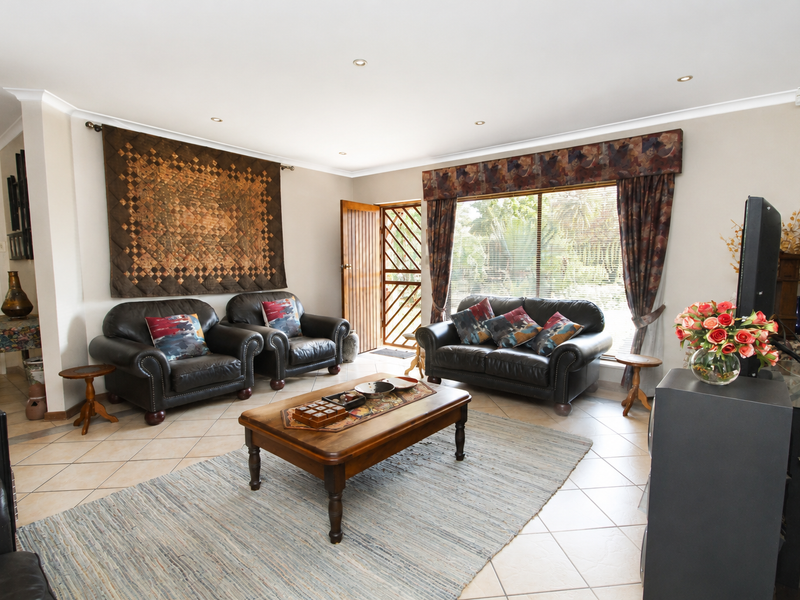 A spacious living room featuring tiled flooring, recessed downlighting, and a large window with a security gate leading to the exterior.