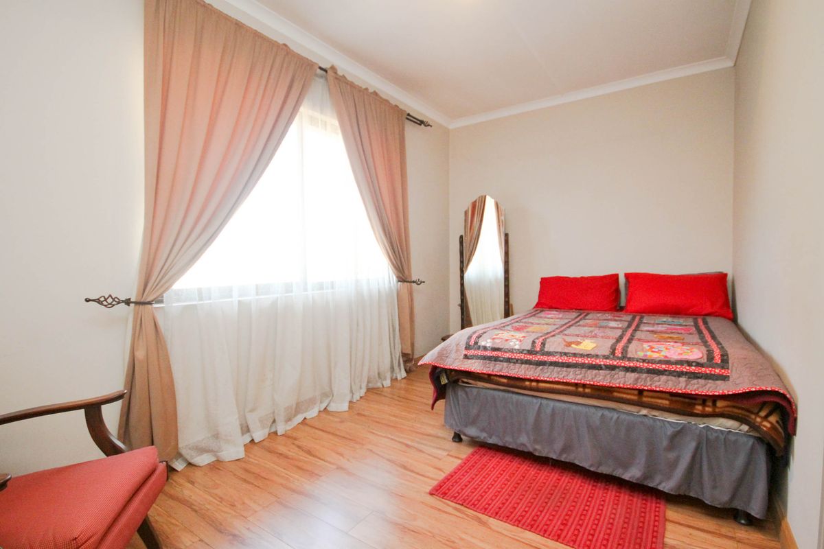 A bedroom featuring laminate flooring and a large window with installed curtain rods.