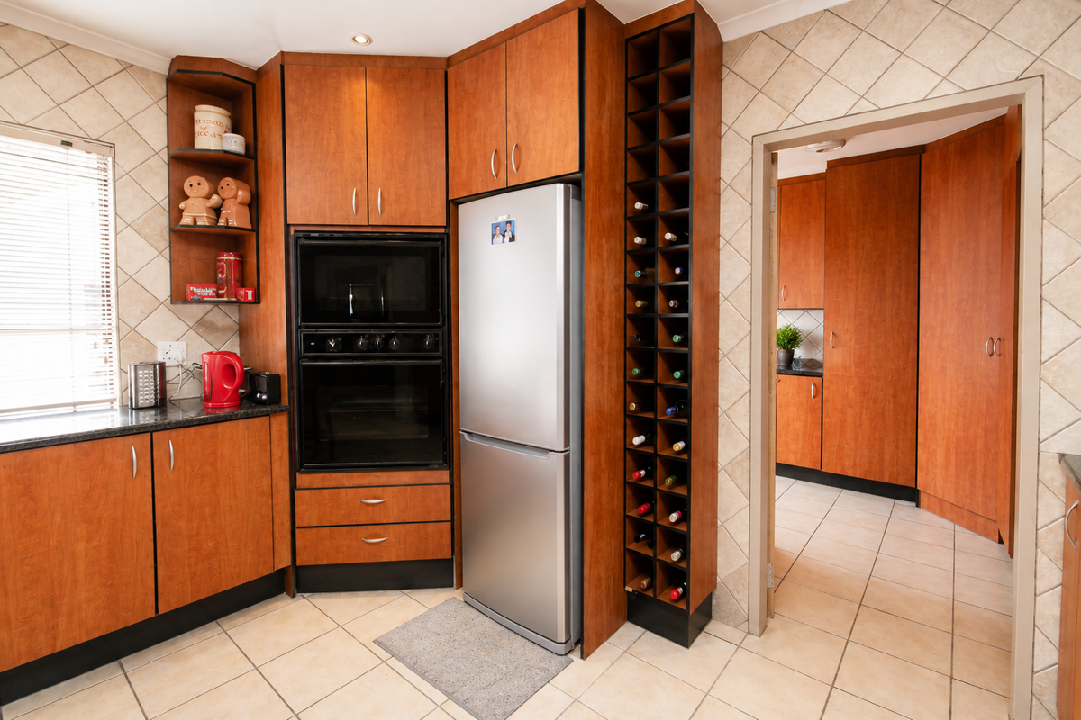 A functional kitchen featuring warm-toned wooden cabinetry, built-in oven and microwave, granite countertops, and a dedicated wine rack, with an adjacent scullery area.