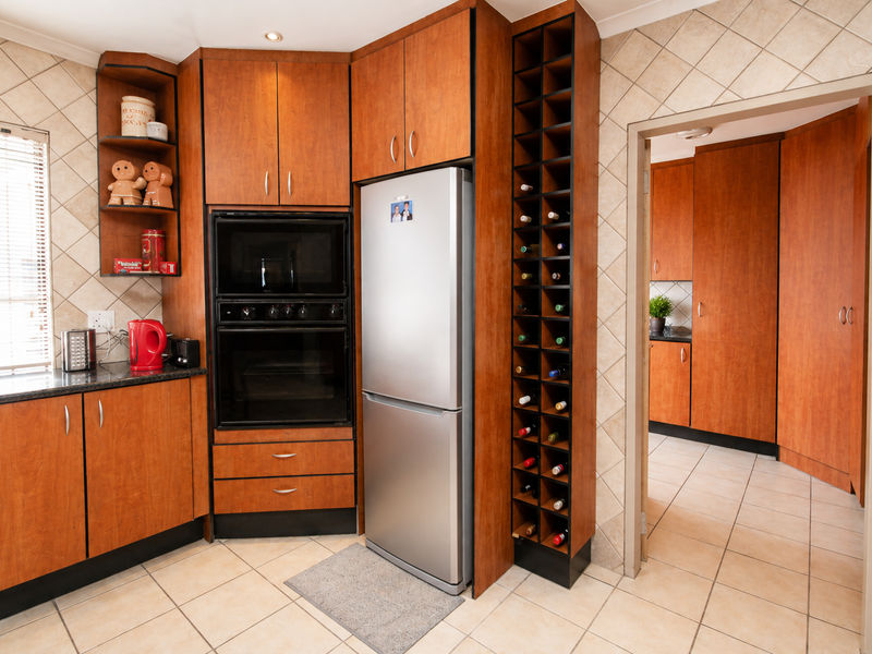 A functional kitchen featuring warm-toned wooden cabinetry, built-in oven and microwave, granite countertops, and a dedicated wine rack, with an adjacent scullery area.
