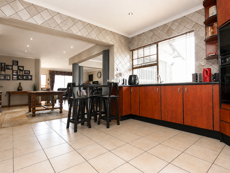 Open-plan kitchen and living area featuring tiled flooring, warm-toned cabinetry, built-in oven, and recessed lighting, creating a functional and connected living space.