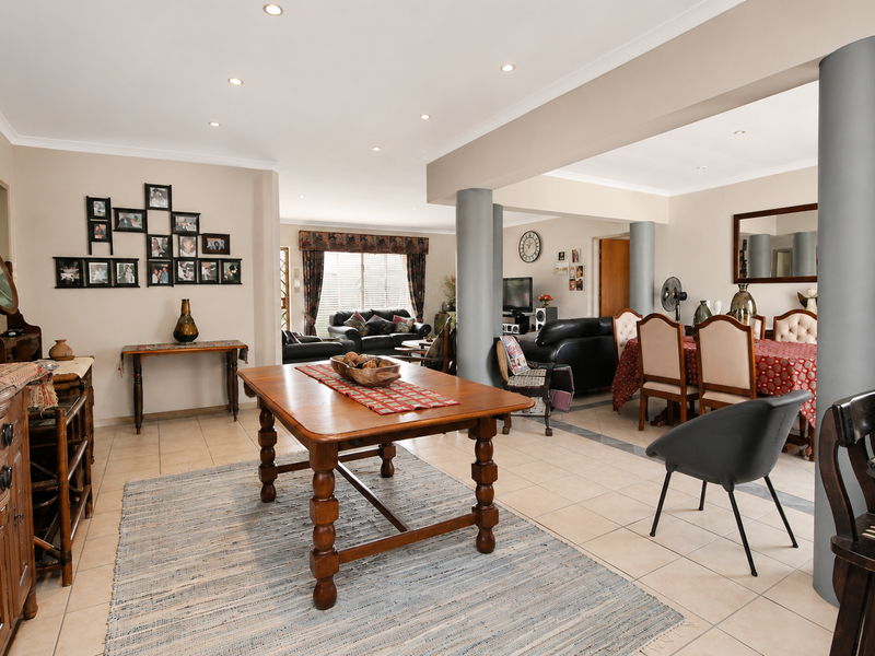 Spacious open-plan living and dining area featuring neutral wall tones, ceramic tiled flooring, and prominent structural support columns with recessed ceiling lighting.
