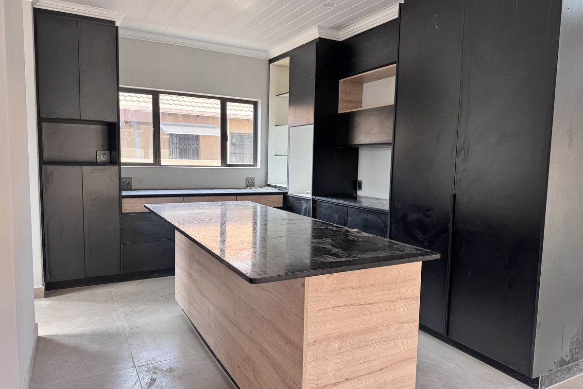 Modern kitchen featuring black cabinetry, a central island with wood-look finish, stone countertops, and tiled flooring in a clean, contemporary space.