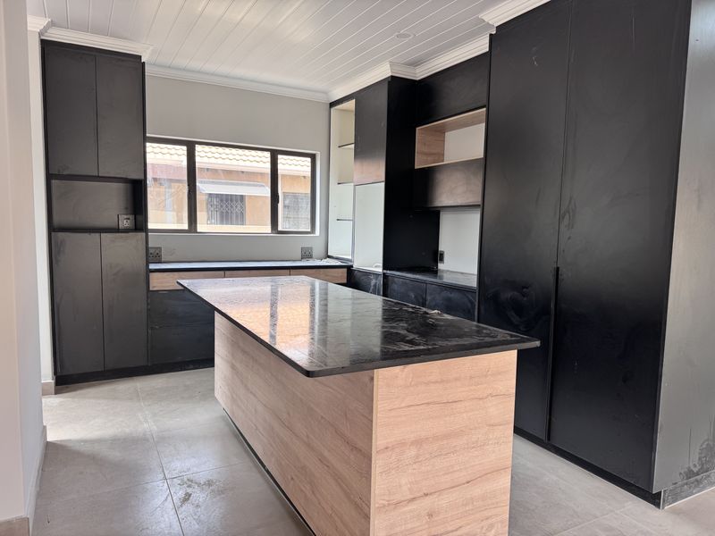 Modern kitchen featuring black cabinetry, a central island with wood-look finish, stone countertops, and tiled flooring in a clean, contemporary space.