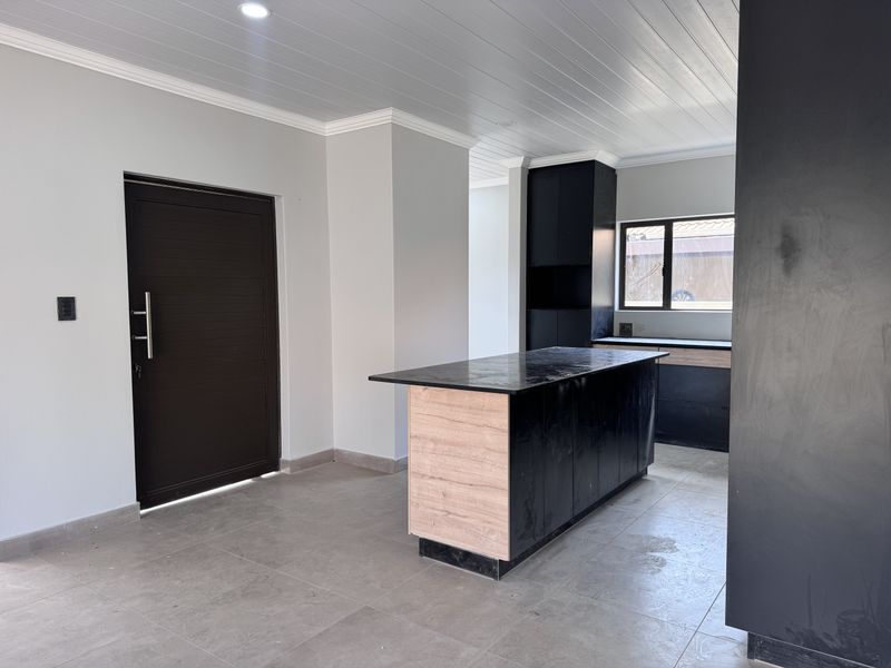 Modern kitchen featuring a central island, dark cabinetry with wood-tone accents, tiled flooring, and recessed lighting in a clean, open-plan layout.
