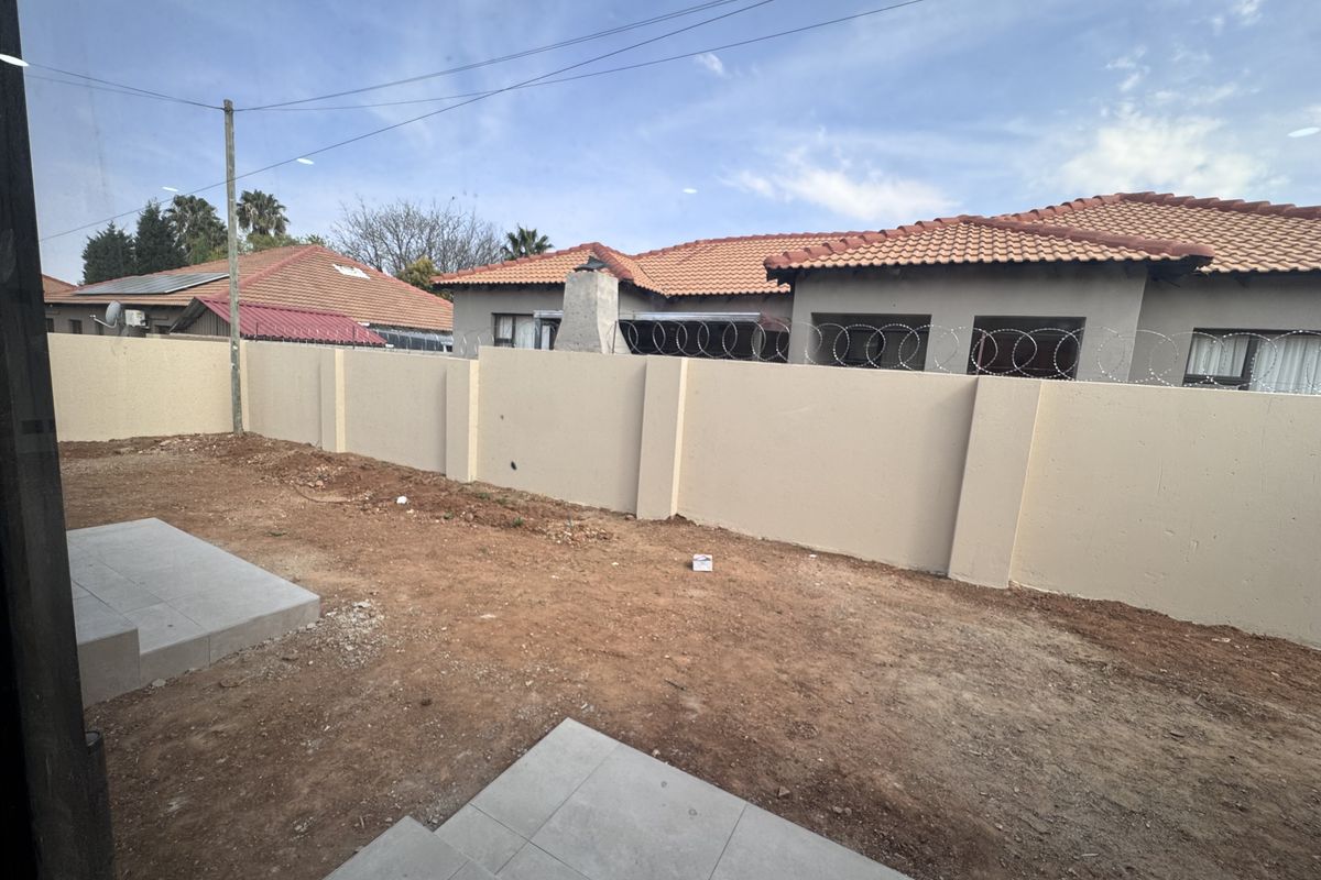Rear exterior view of the townhouse featuring a perimeter wall with security razor wire and unfinished garden space with tiled patio steps.