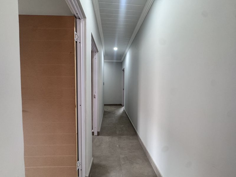 A clean, empty hallway featuring tiled flooring, recessed downlighting, and timber veneer doors, providing access to multiple rooms within the townhouse.