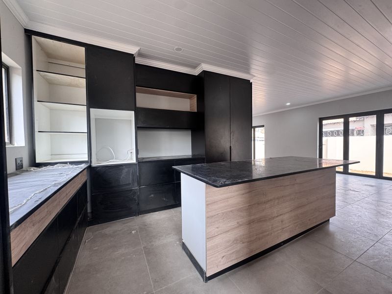 Modern open-plan kitchen featuring a central island, dark cabinetry, and stone countertops, currently in an unfinished state awaiting final installation and completion.
