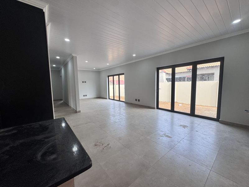 Spacious open-plan living area featuring modern tiled flooring, recessed lighting, and large black aluminium stacker doors providing access to the exterior.
