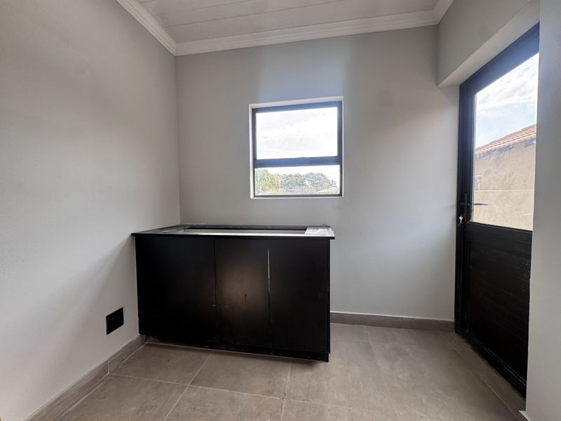 A clean, empty laundry or utility space featuring dark built-in cabinetry, tiled flooring, and direct access to the exterior.