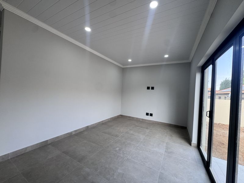 A bright, empty living room featuring modern grey floor tiles, recessed ceiling lighting, and large sliding glass doors providing access to the exterior.