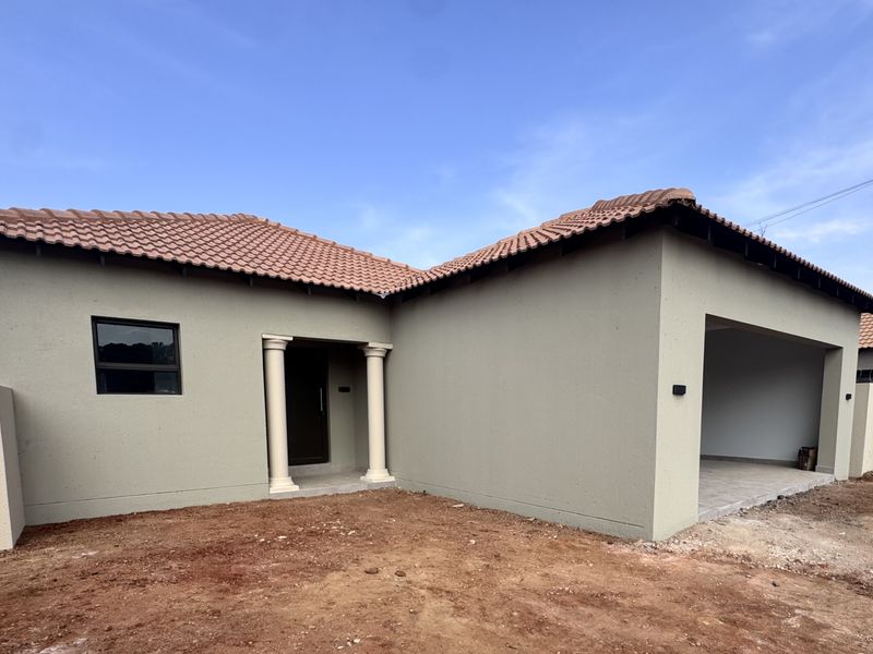 Front elevation of a modern townhouse featuring a tiled roof, covered entrance with decorative columns, and an open garage bay with unfinished landscaping.
