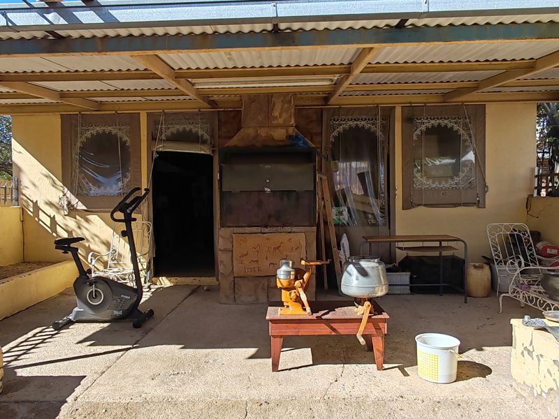 Covered outdoor patio area featuring a built-in braai, concrete flooring, and corrugated metal roofing, requiring maintenance and cosmetic updates.