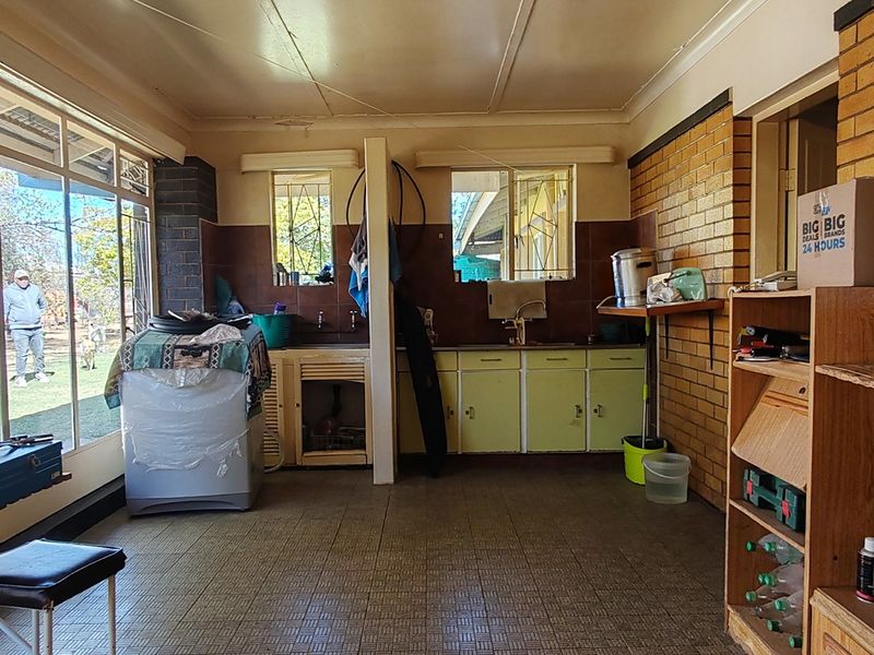 A functional scullery area featuring built-in cabinetry, a sink, and large windows overlooking the garden, with exposed brick walls and tiled flooring.