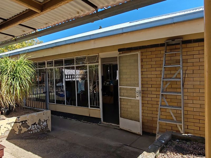 A covered outdoor patio area featuring brick walls, concrete flooring, and raised planter boxes, showing signs of wear and requiring maintenance.