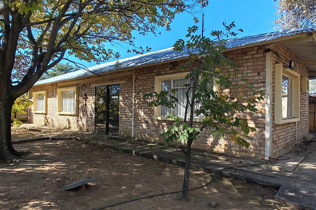 Rear view of a single-story face brick house featuring a corrugated metal roof, sliding glass door access, and a surrounding garden area.