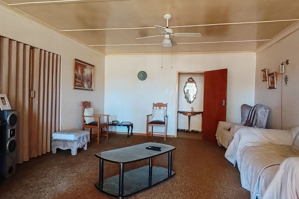 Spacious living room featuring a ceiling fan, panelled ceiling, and carpeted flooring, offering a dated interior ready for modern updates.