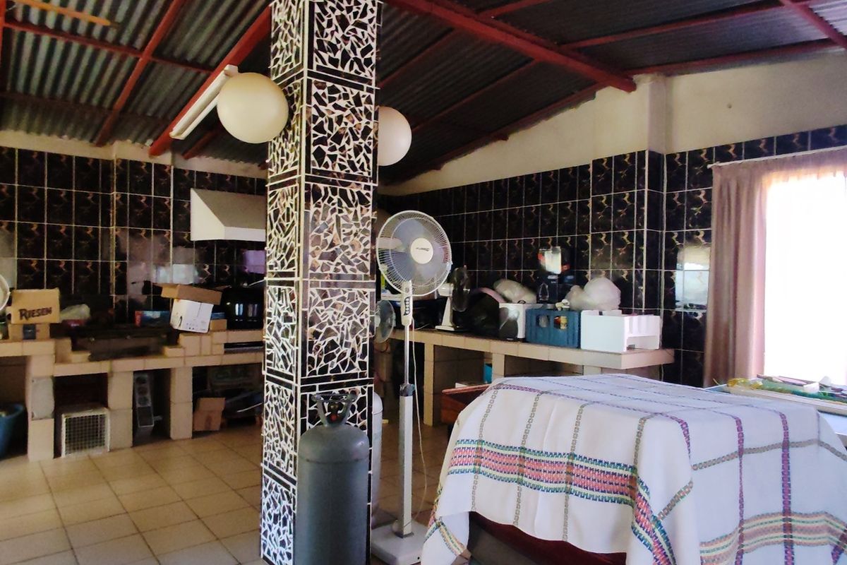 A rustic kitchen area featuring masonry counters, dark tiled walls, and an exposed corrugated metal roof structure.