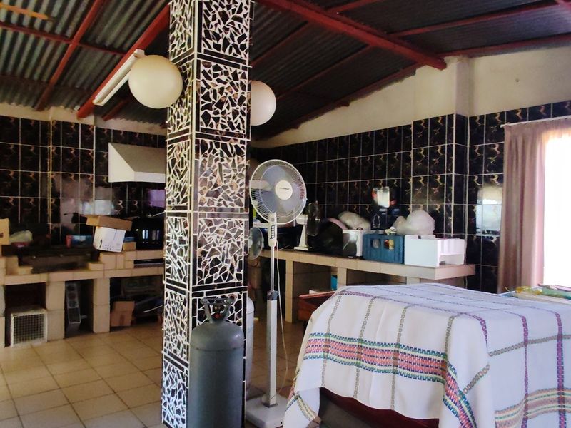A rustic kitchen area featuring masonry counters, dark tiled walls, and an exposed corrugated metal roof structure.