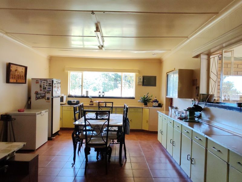 Spacious open-plan kitchen and dining area featuring extensive built-in cabinetry, tiled flooring, and a large pass-through window connecting to an adjacent space.
