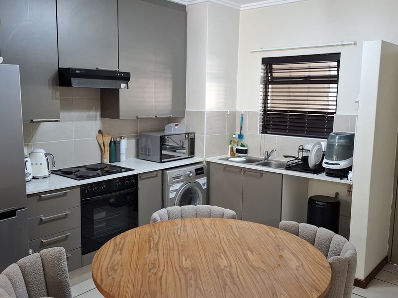 Modern kitchen featuring grey cabinetry, built-in oven and hob, extractor fan, and a double sink with tiled backsplash and flooring.