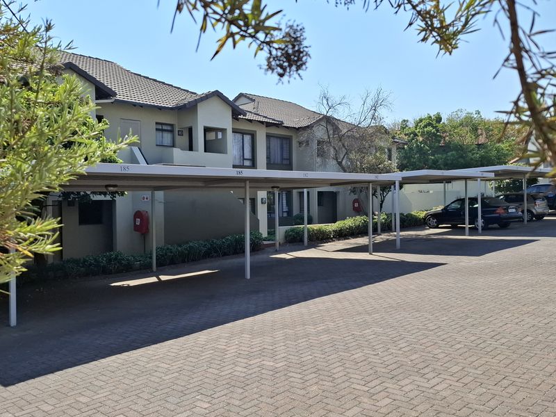 Exterior view of the apartment complex featuring a paved driveway and covered parking bays for residents.