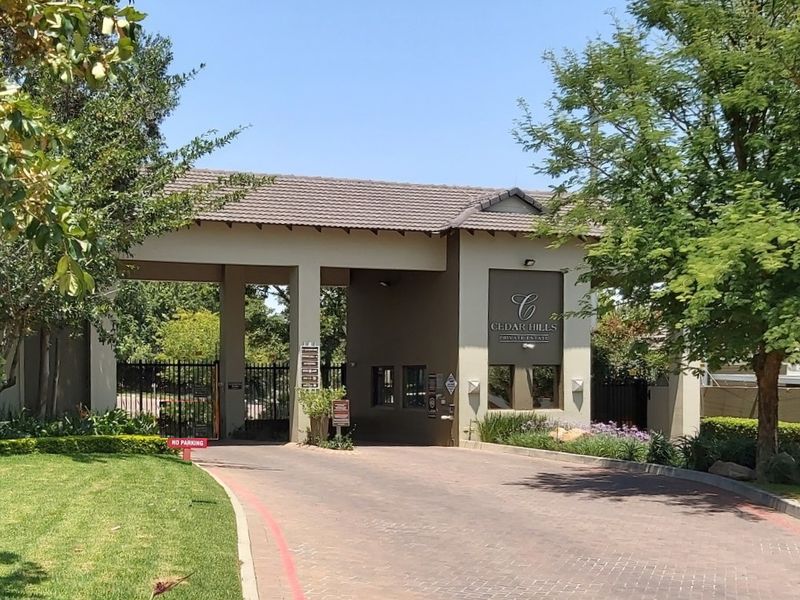 The main entrance gate and guard house of Cedar Hills Private Estate, featuring a paved driveway and well-maintained landscaping.