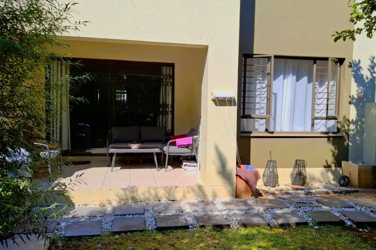 Rear view of the apartment featuring a covered tiled patio, sliding glass doors with security gates, and a landscaped garden area with paver stones.