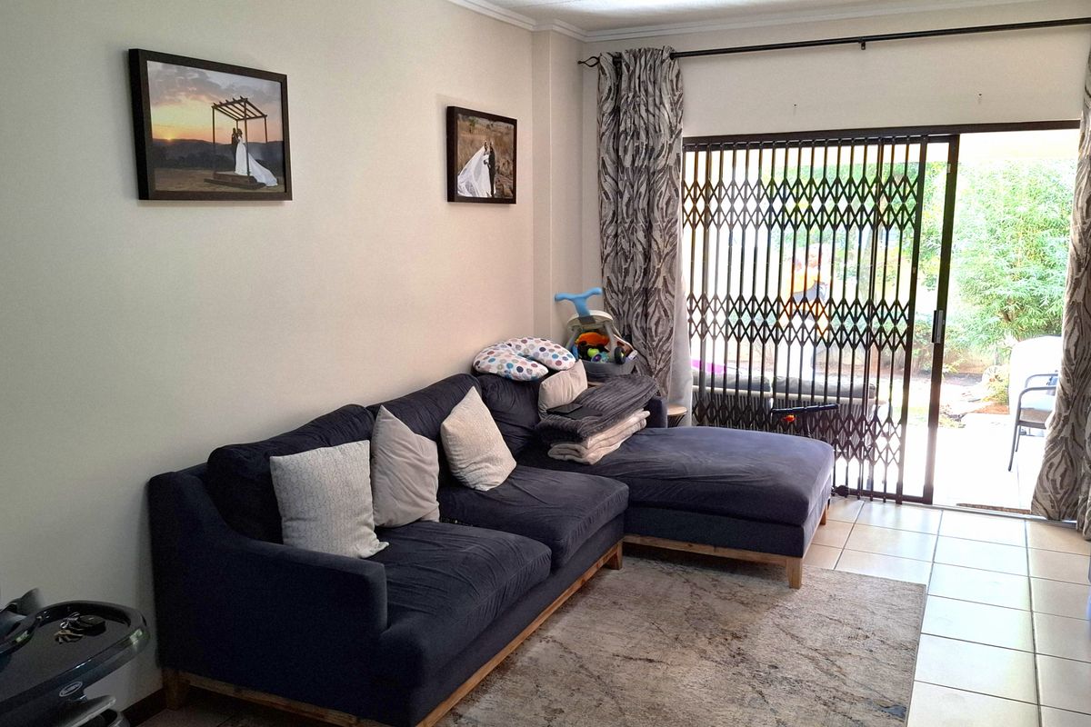 A comfortable living room featuring tiled flooring and a sliding glass door with a security gate, providing direct access to the outdoor area.
