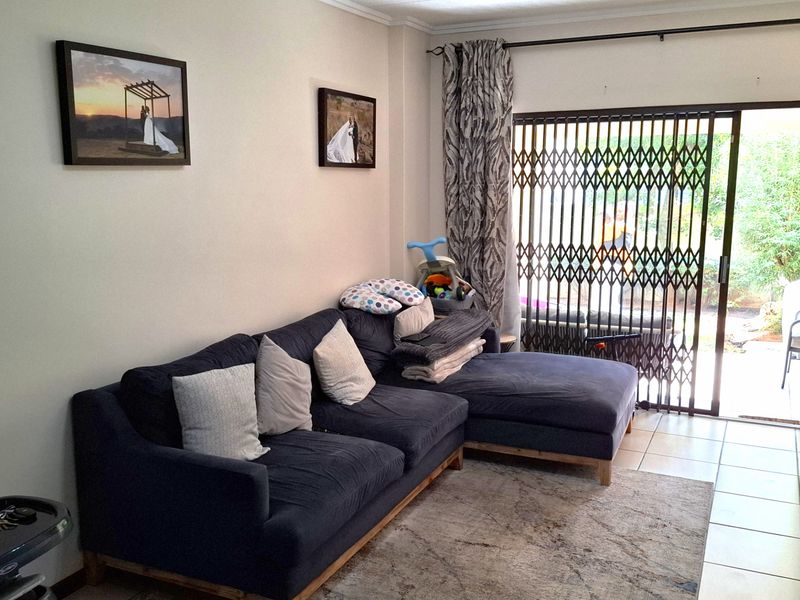 A comfortable living room featuring tiled flooring and a sliding glass door with a security gate, providing direct access to the outdoor area.