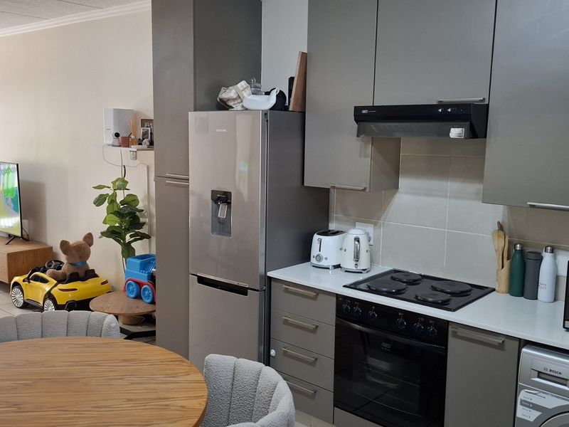 Open-plan living area featuring a modern kitchen with grey cabinetry, electric hob, built-in oven, and integrated laundry appliances, flowing into the lounge space.
