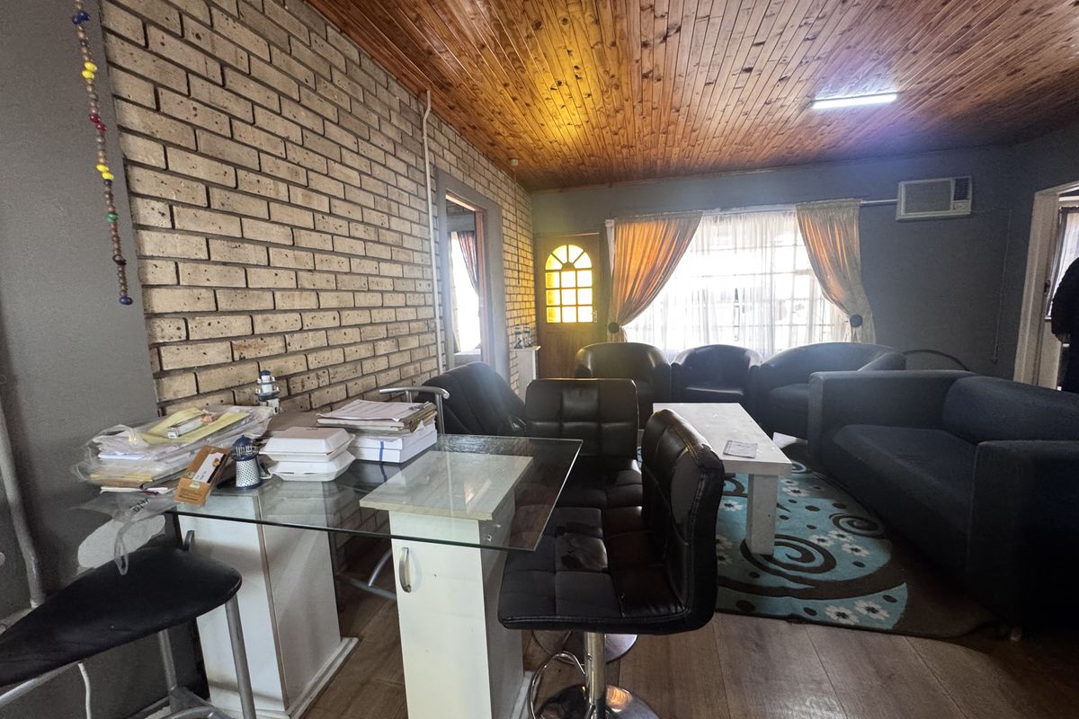 A living room featuring an exposed brick wall, timber ceiling, and laminate flooring, offering a rustic aesthetic with potential for modern updates.