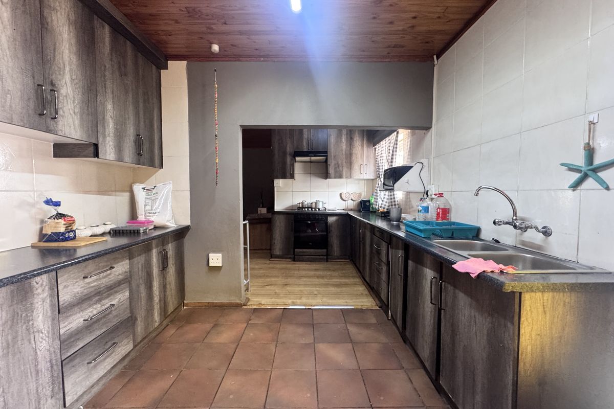 A functional kitchen featuring dark wood-look cabinetry, laminate countertops, a double basin sink, and integrated cooking appliances with a timber-paneled ceiling.