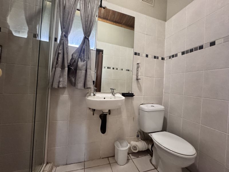 A functional bathroom featuring a wall-mounted basin, dual-flush toilet, and a glass-enclosed shower with neutral wall tiling.