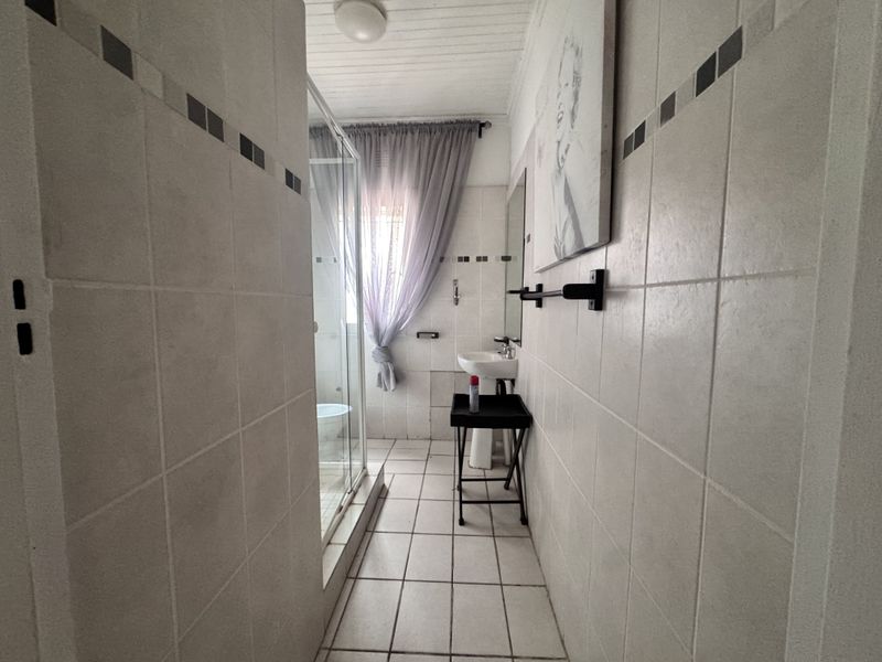 A functional bathroom featuring a pedestal basin, a glass-enclosed shower, and neutral wall and floor tiling.